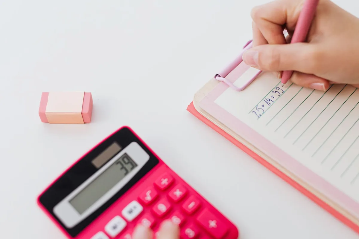 Hands writing in a notebook beside a calculator