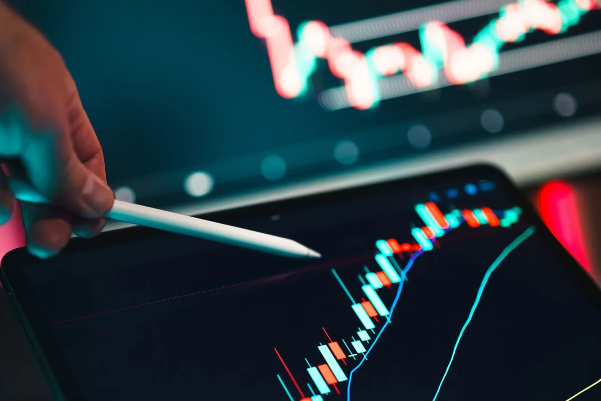 A stylus pointing at a candlestick chart on a tablet screen